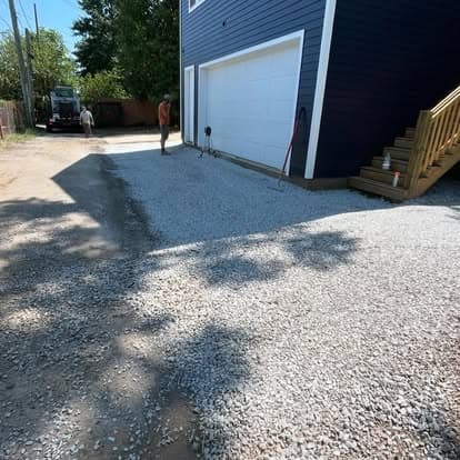 Gravel driveway installation near a blue house with new stairs and garage.