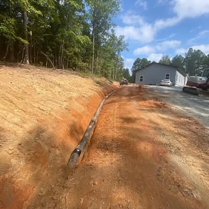 Excavated trench with utility pipe installation beside construction site in wooded area.