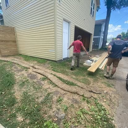 Workers transporting lumber near a house with new siding and a freshly landscaped yard.