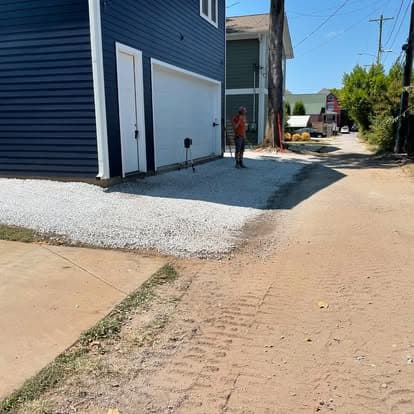New gravel driveway and blue house in a suburban area, with a person working nearby.
