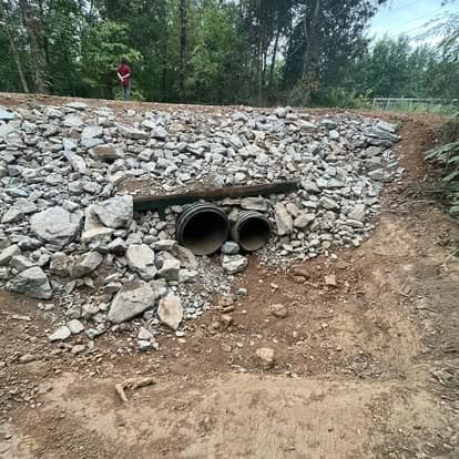 Drainage pipes surrounded by gravel and rocks in a natural setting with trees.