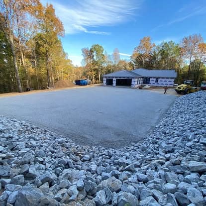 Newly gravelled construction site with a house in progress and autumn foliage nearby.