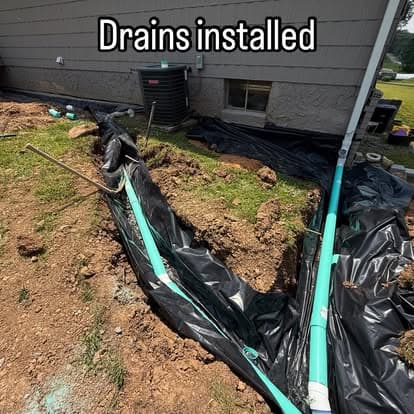 Drains installed in yard with black landscaping fabric and green piping for effective drainage.