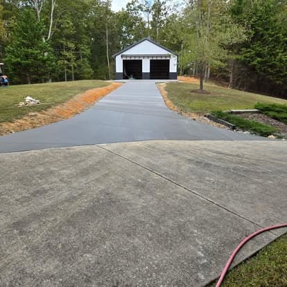 Concrete driveway leading to a white garage surrounded by lush greenery and landscaping.