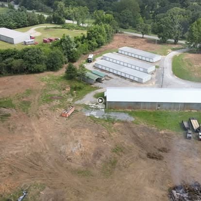 Aerial view of a cleared land with storage buildings and surrounding greenery.