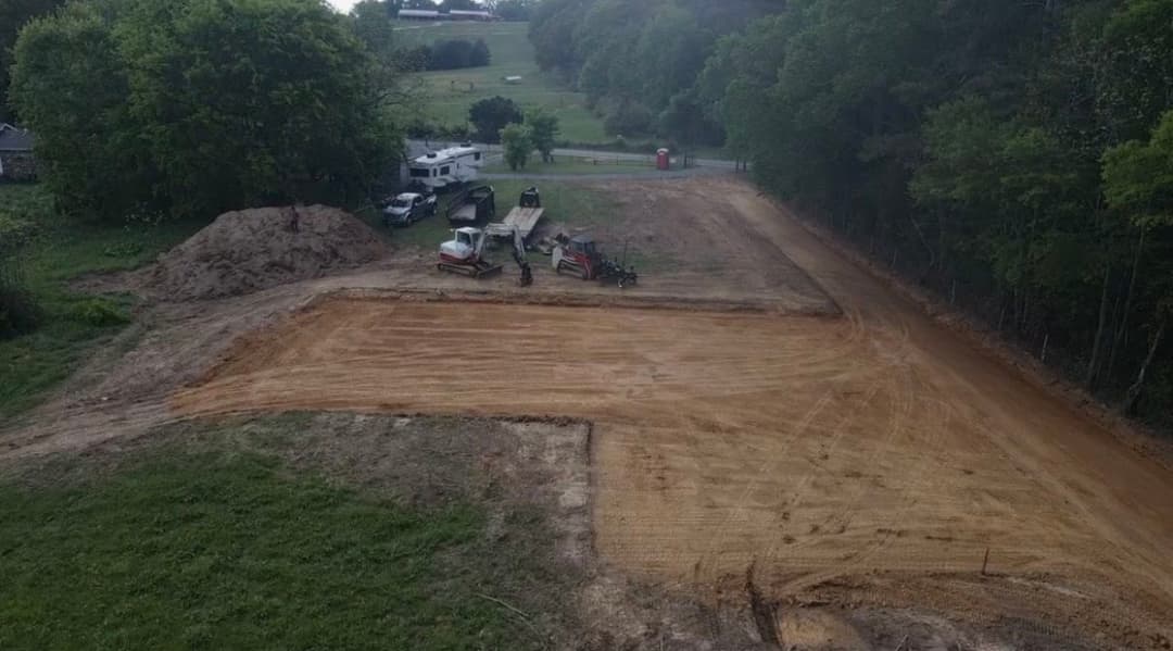 Construction site with machinery clearing land and preparing a foundation in a rural area.