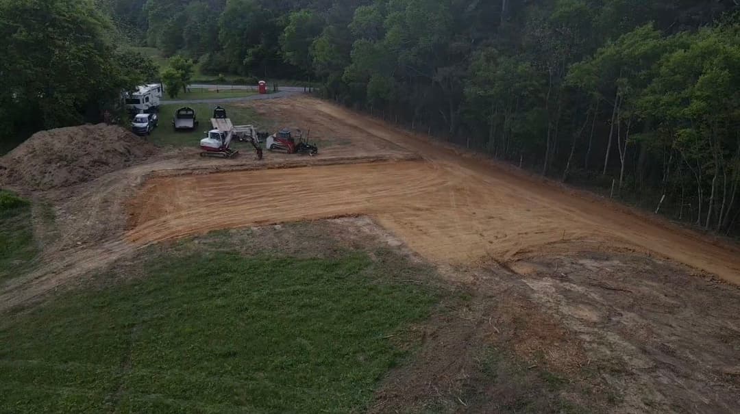 Aerial view of construction site with machinery on dirt clearing, surrounded by trees.