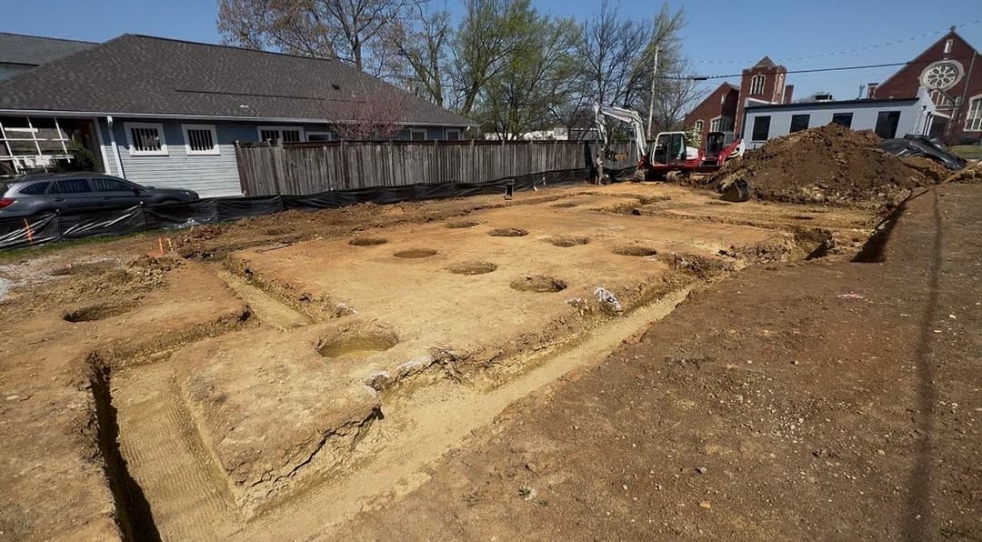 Excavation site with circular foundation holes and construction equipment in a suburban area.