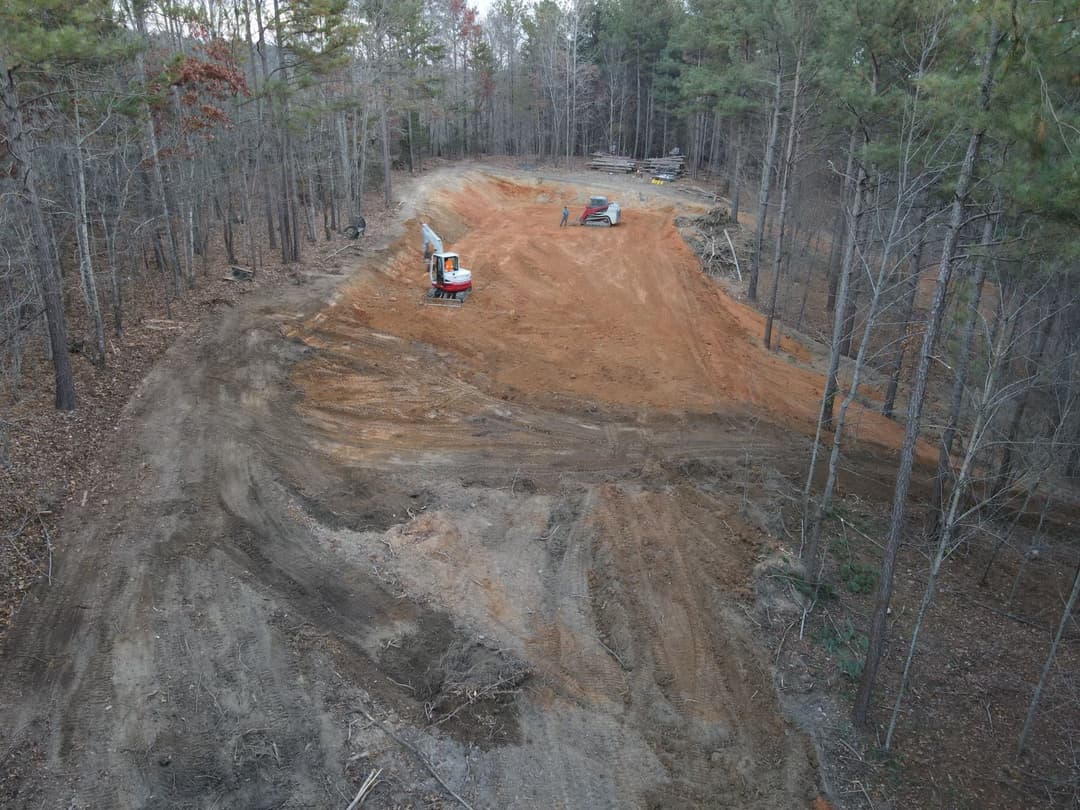 Aerial view of cleared land with heavy machinery in a wooded area preparing for construction.