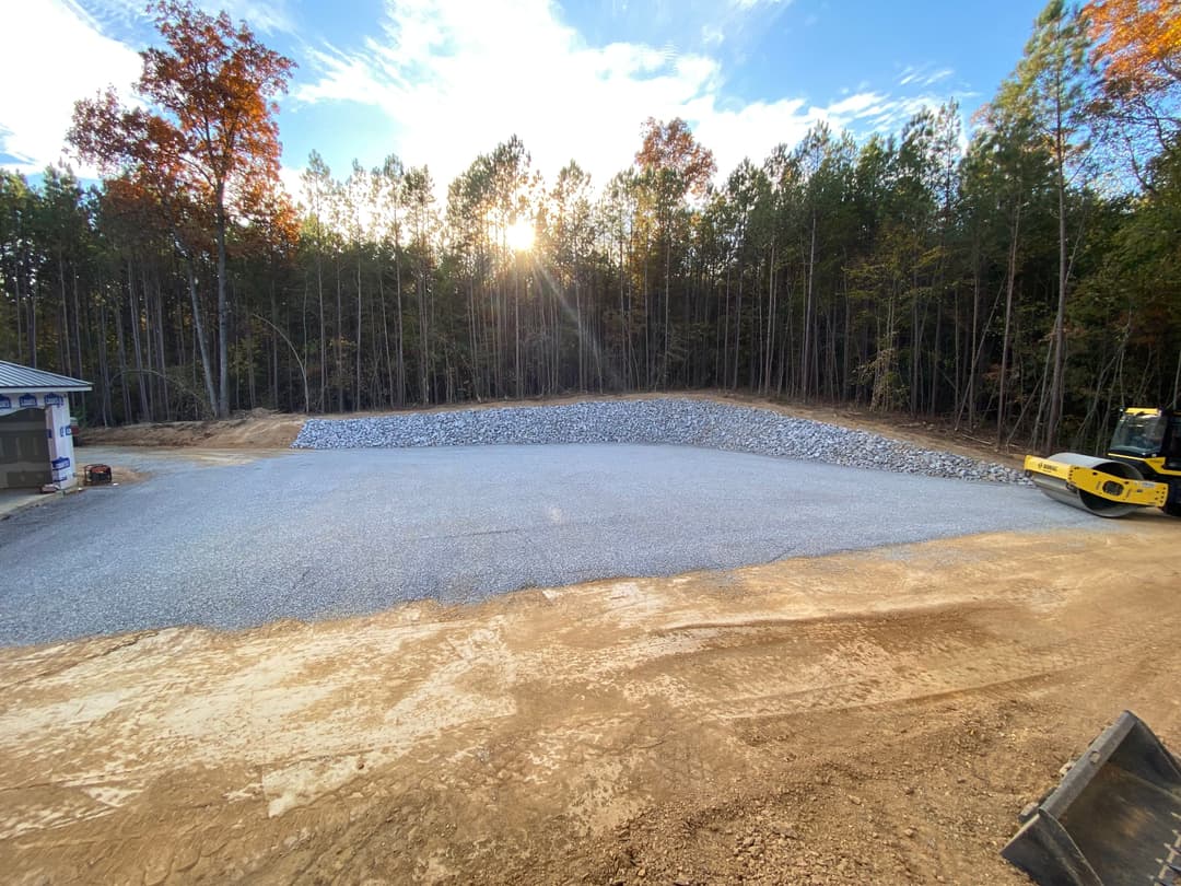 Gravel base prepared for construction project in wooded area with trees and sunset.