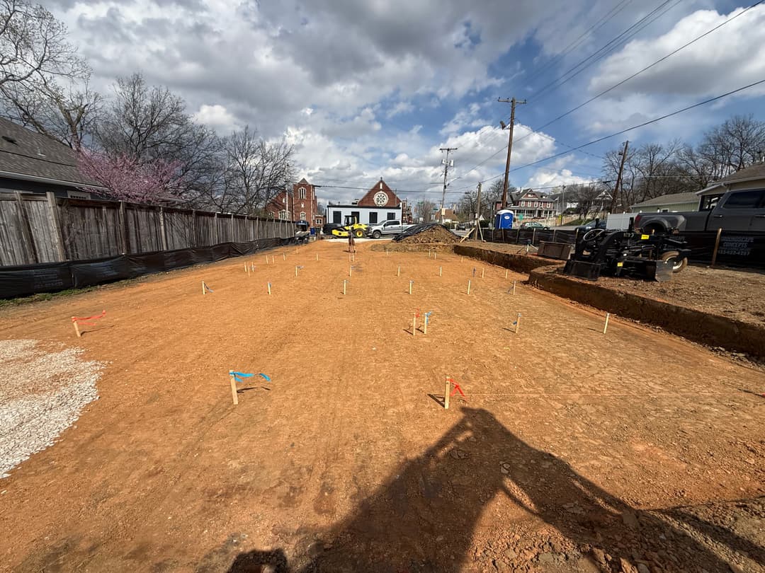 Construction site with marked foundation area and tools under a cloudy sky.
